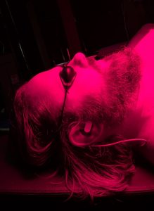 Man laying with red light shining on face, wearing goggles and vagus nerve stimulator.